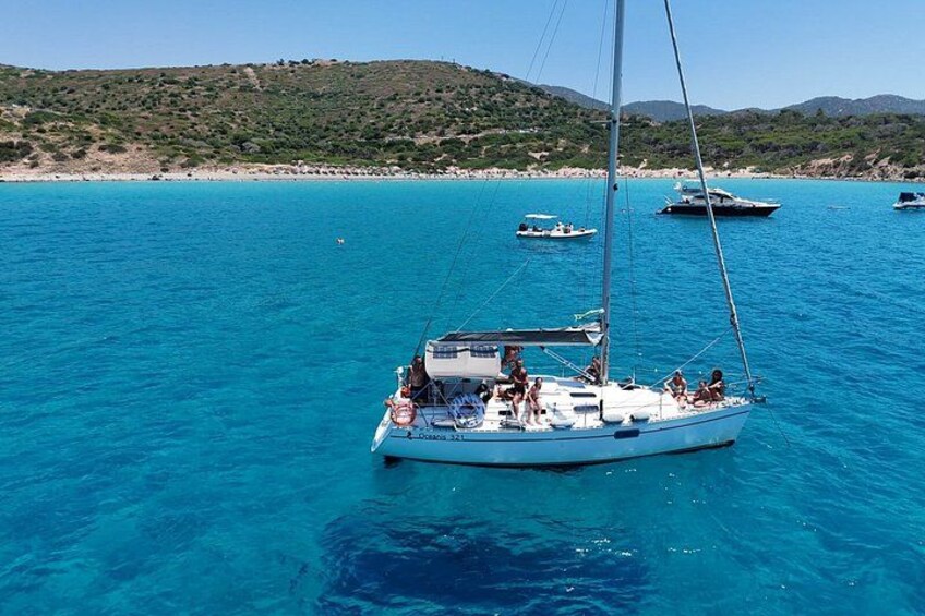 A sailboat on a turquoise sea with a beach and hills in the background. 1