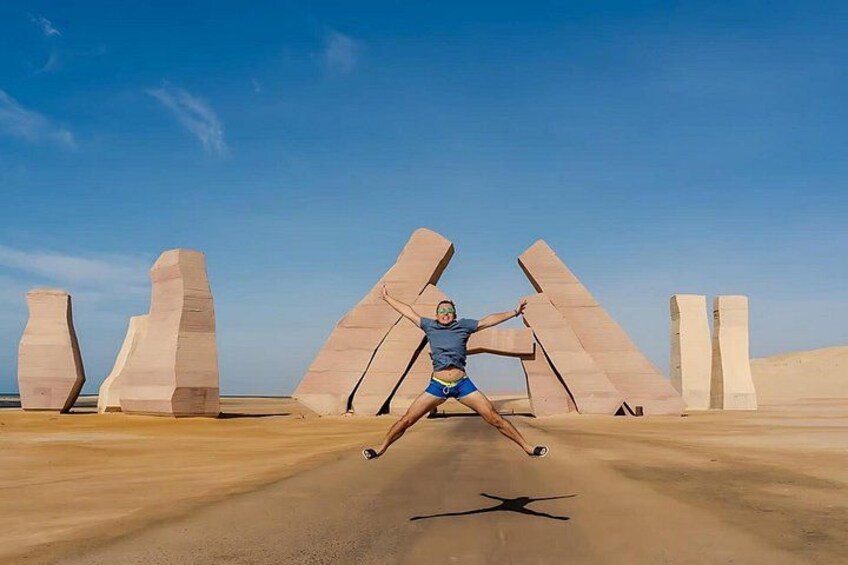 Una persona bailando en un desierto con esculturas abstractas de gran tamaño al fondo. 1