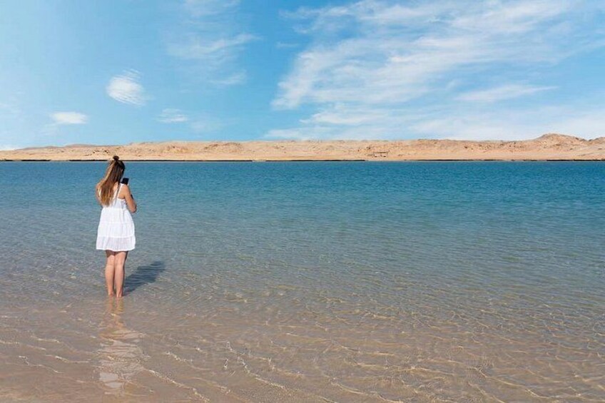 Una persona con un vestido blanco parada en aguas poco profundas, con un paisaje desértico al fondo. 5