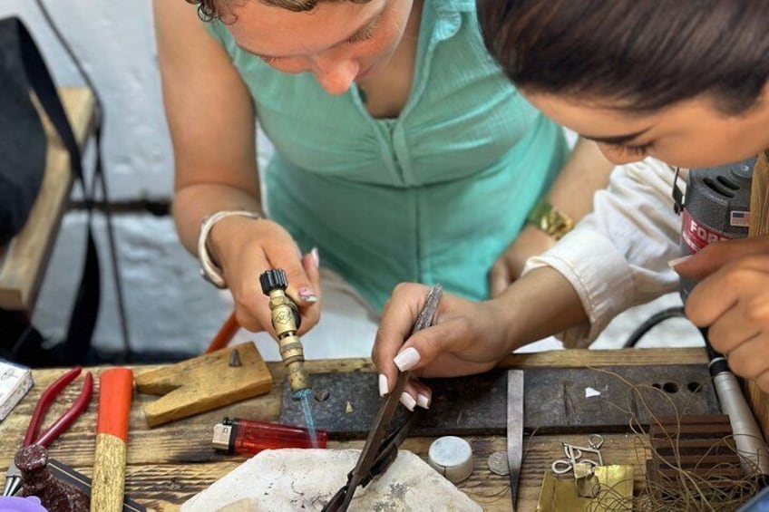 Two people working with tools on a wooden surface, surrounded by various items like pliers, a hammer, and a drill. 3