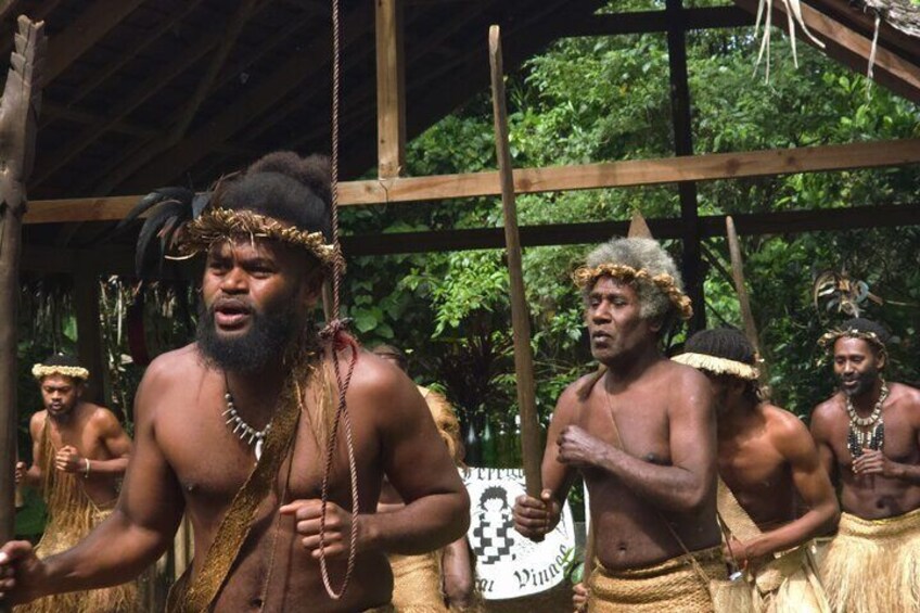 A group of people in traditional attire, standing under a wooden structure in a forested area. 5