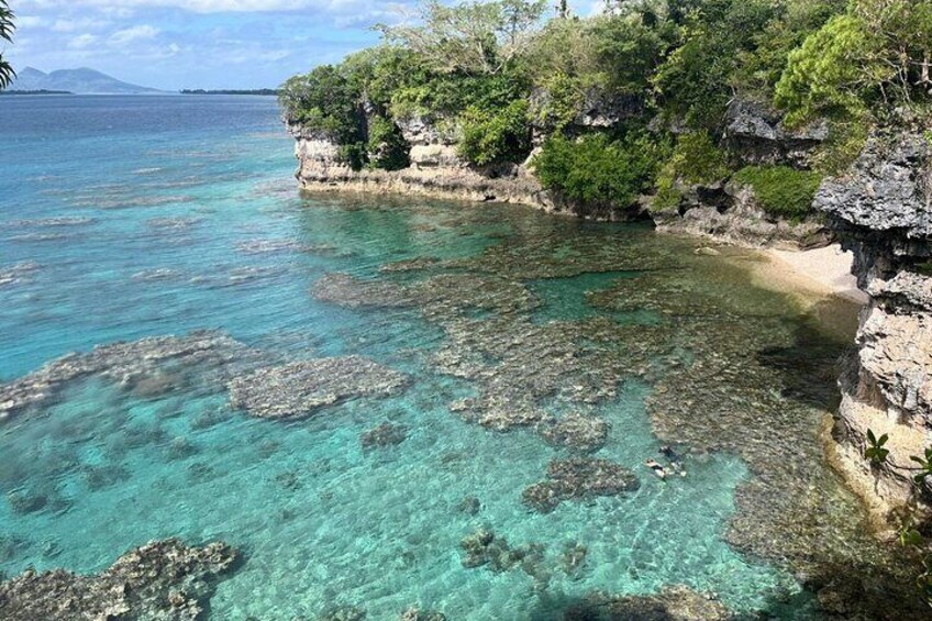 A coastal landscape with clear turquoise waters, rocky formations, and lush greenery. 2