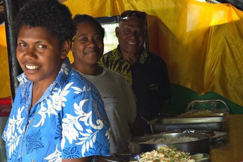 People standing in front of a food stall with dishes of food. 3