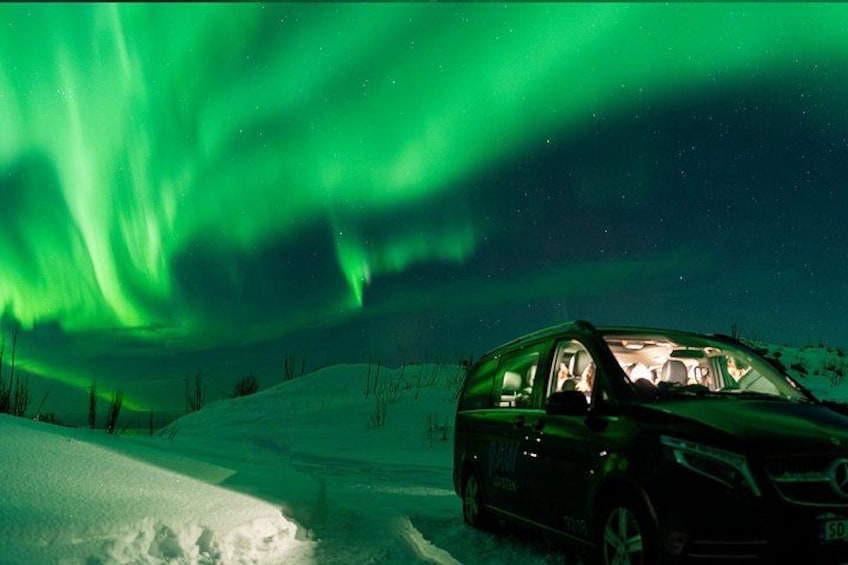 A vehicle parked in a snowy landscape under a green aurora. 4