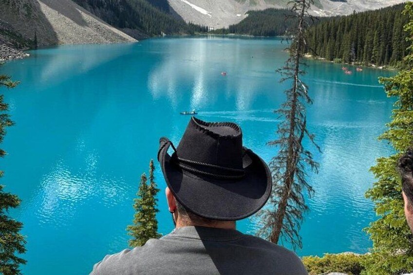 A person wearing a black hat and gray shirt, overlooking a turquoise lake with mountains in the background. 2