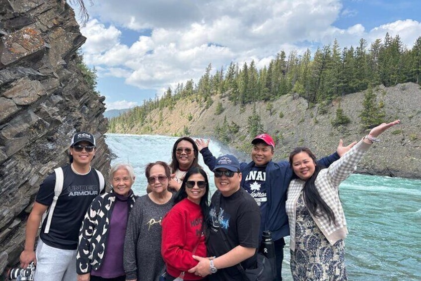 A group of people standing by a river with a waterfall in the background. 5
