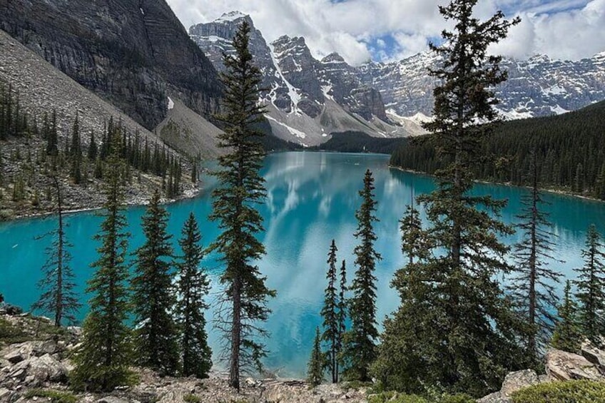 A turquoise lake surrounded by coniferous trees and mountains with snow-capped peaks. 4