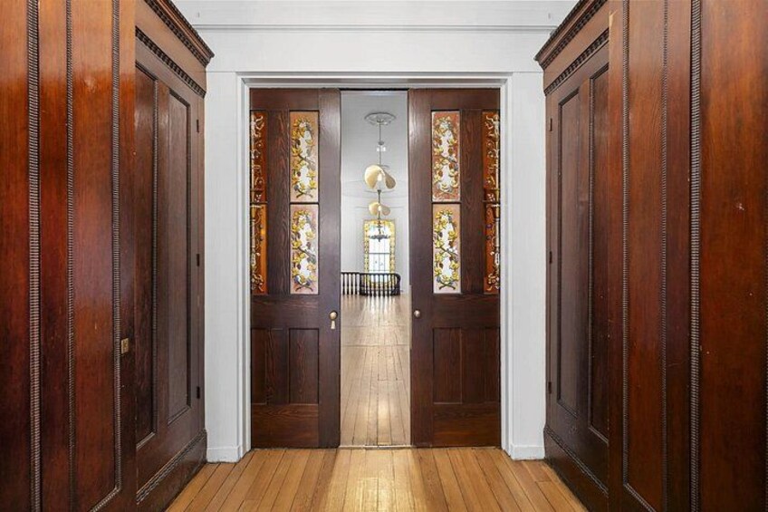 Un couloir en bois orné d’un lustre, doté de portes en bois et d’une fenêtre en verre décoré de motifs. 2