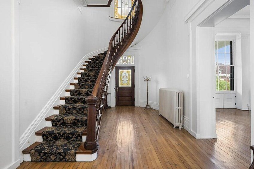 Un escalier en bois, dont les marches sont recouvertes de moquette, mène à une porte ornée d’un vitrail. 3