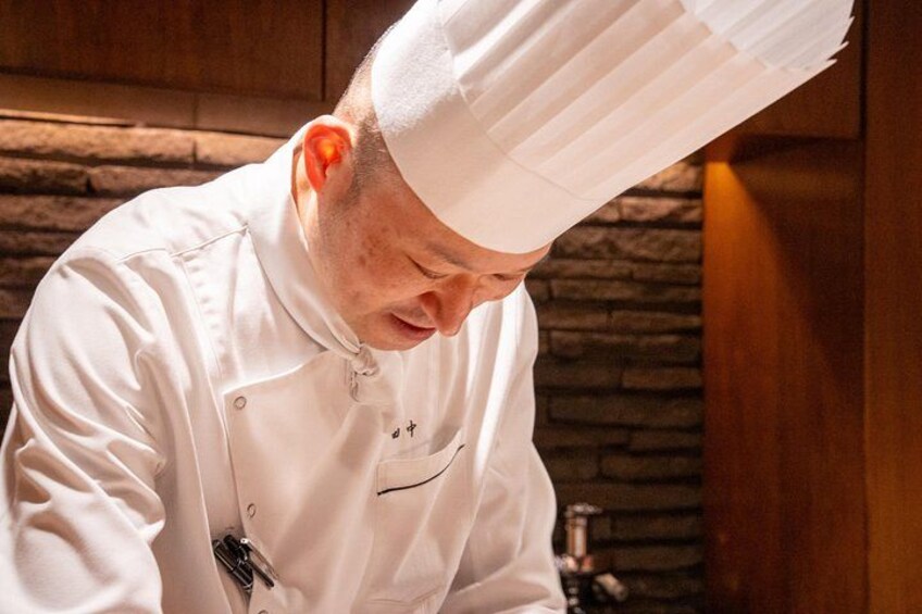 Un chef con uniforme blanco y un alto gorro blanco, concentrado en la cocina. 2