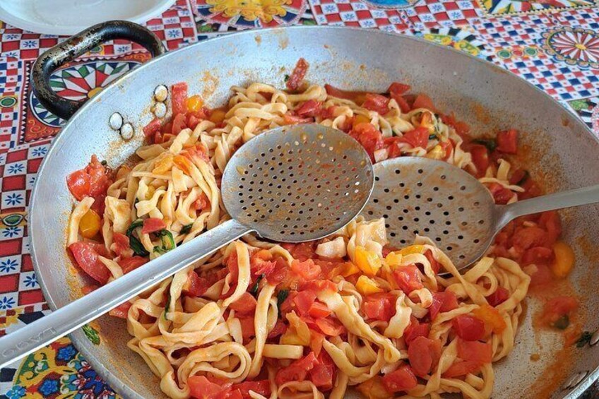 A pan with pasta and vegetables, a ladle, and a colorful tablecloth. 5