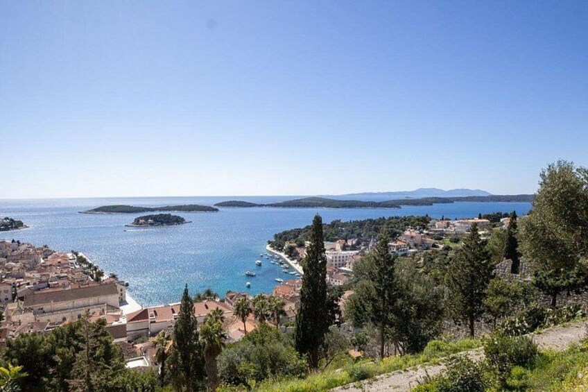 A coastal town with a clear blue sea, a small island, and a hilly landscape with trees. 4