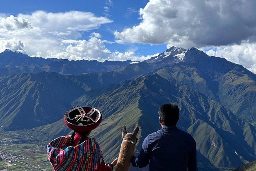 A person wearing a colorful hat and a patterned shirt, pointing towards a mountain range with a clear sky. 4