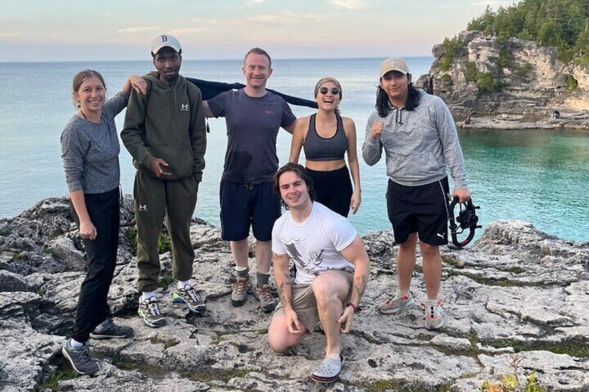 A group of people standing on rocky terrain by a body of water. 1