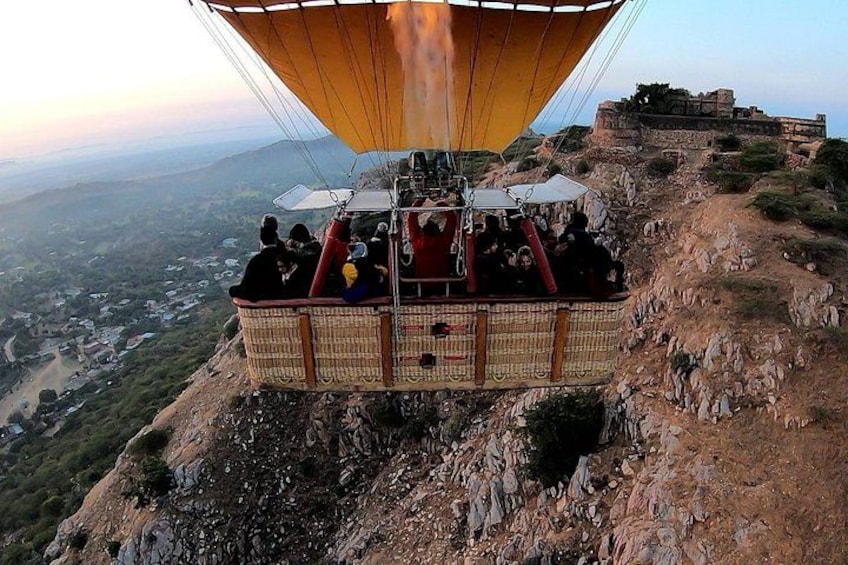 A wicker basket suspended by a cable, with a group of people inside, overlooking a landscape with a distant building. 4