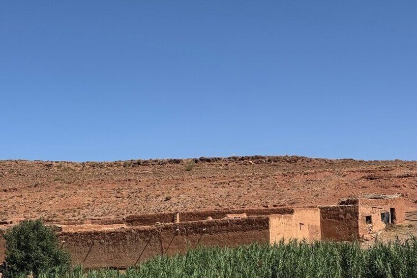 A desert landscape with reddish soil, a small building, and sparse vegetation. 3