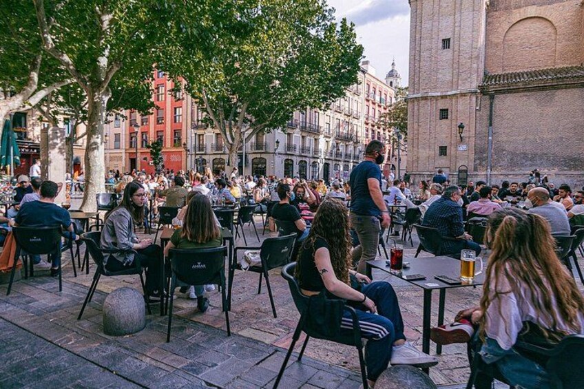 A crowded outdoor café with people sitting at tables, surrounded by trees and buildings. 4