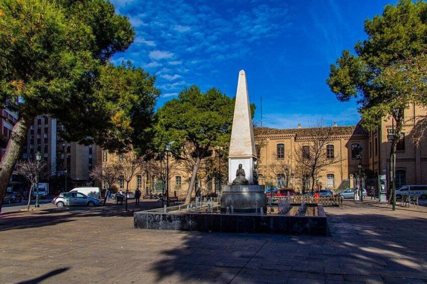 A public square with a central obelisk monument, surrounded by trees and buildings. 5
