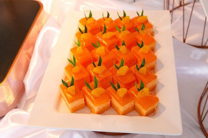 En vit, rektangulär tallrik med orangefärgade matbitar och gröna blad, arrangerade i rader. 3