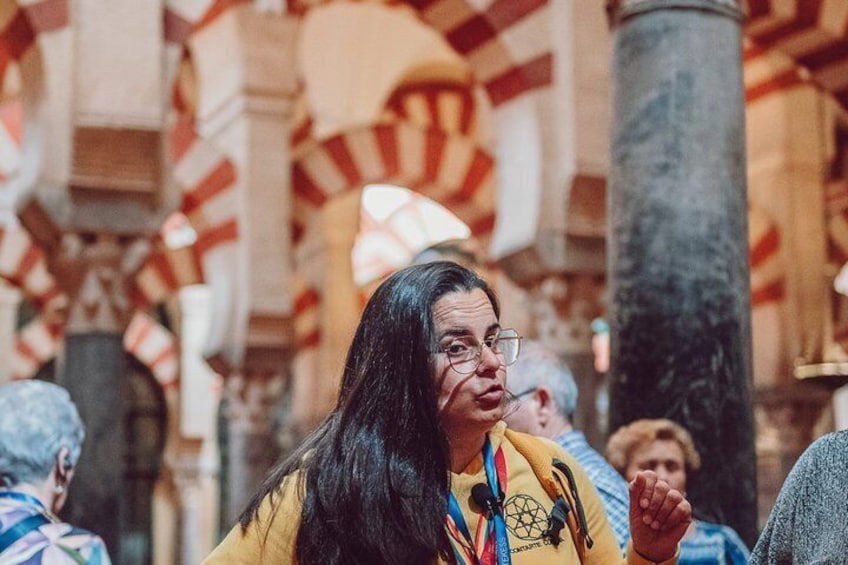 A person in a yellow shirt with a colorful scarf in a historic building with red and white striped arches. 1