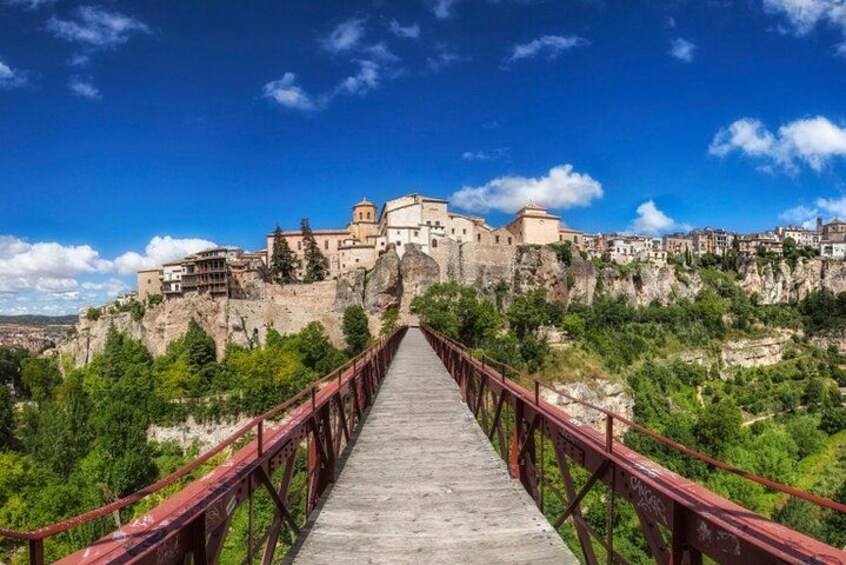 A wooden bridge leading to a historic city with buildings on a rocky hill. 2