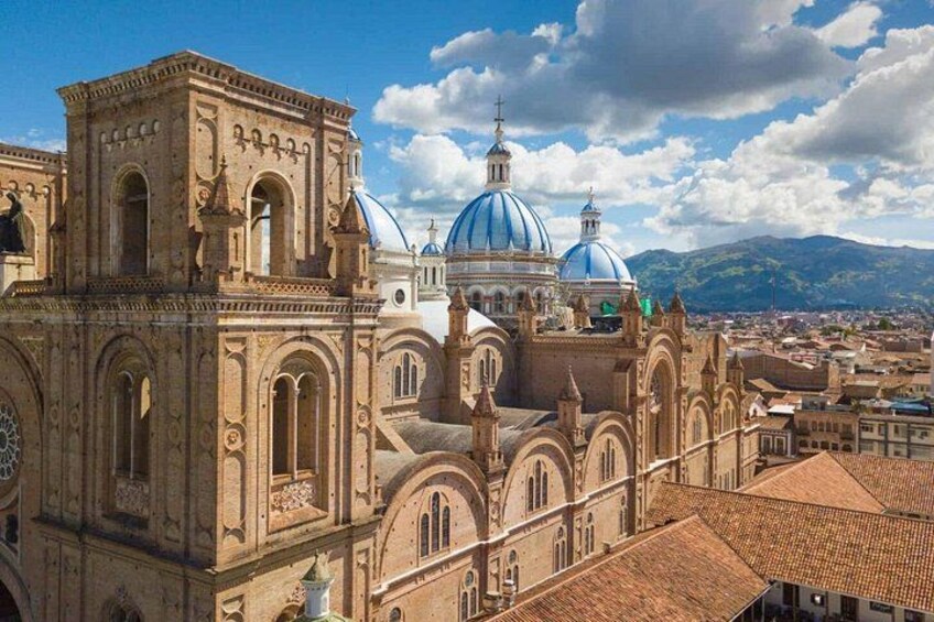 A historic church with ornate architecture and blue domes, surrounded by a cityscape and mountains in the background. 4
