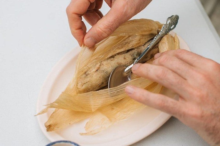 A person cutting a tamale with a knife on a plate. 3