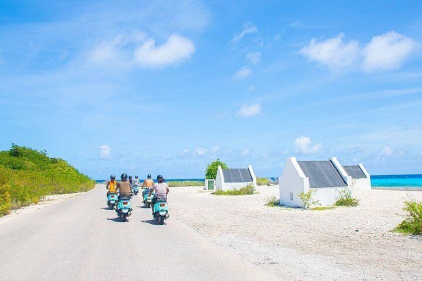 A road with motorcyclists, beach huts, and the ocean. 4