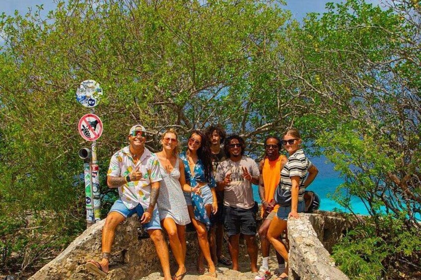 A group of people posing on a rocky ledge with a body of water and trees in the background. 1