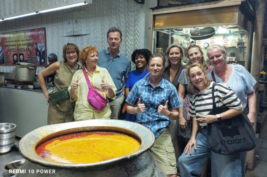A group of people in a kitchen with a large pot on the counter. 4