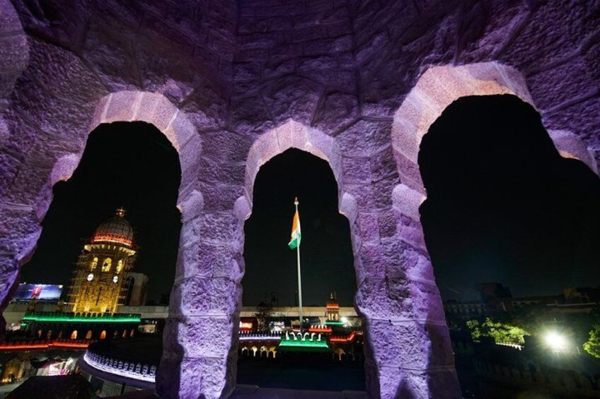 A nighttime view of a historic archway with a flagpole in the center, illuminated by artificial lighting. 2