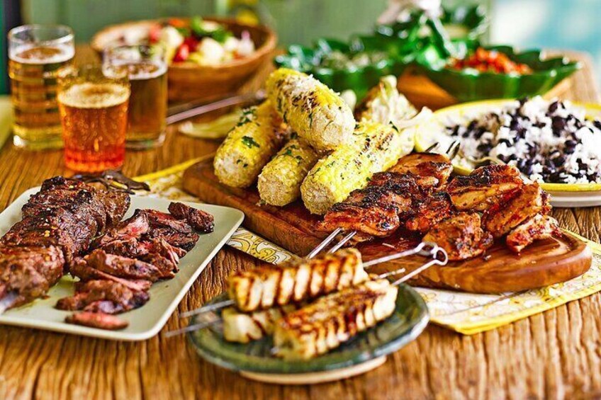 A variety of grilled meats, corn on the cob, and rice dishes on a wooden table. 1