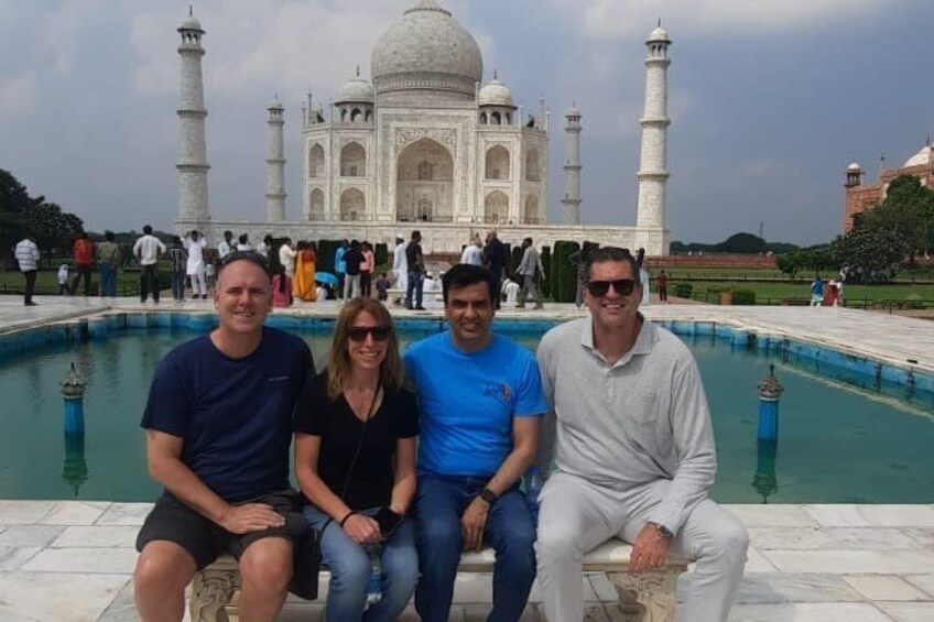 Drei Personen sitzen auf einer Bank, im Hintergrund der Taj Mahal. 2