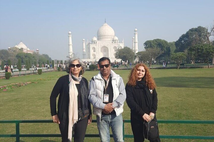 Drei Personen vor dem Taj Mahal, im Vordergrund ein grüner Zaun. 1
