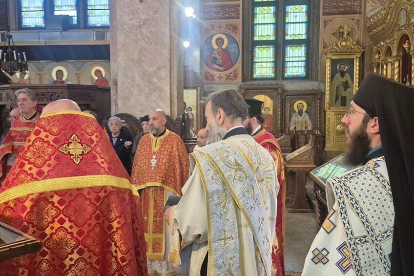A group of clergy in ornate robes inside a church with religious icons and stained glass windows. 2
