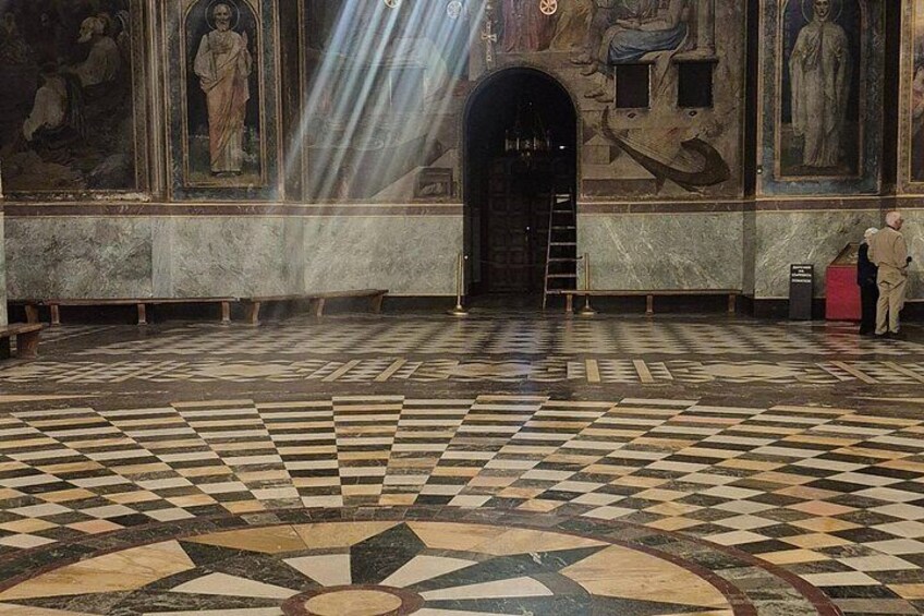 A large hall with a checkered floor, a dark doorway, and frescoes on the walls. 4