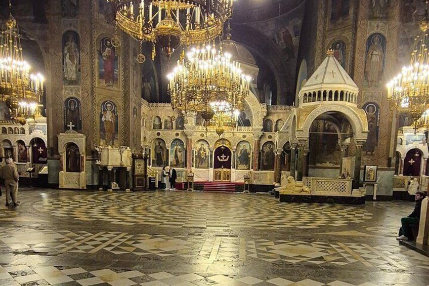 An ornate church interior with chandeliers, religious icons, and a patterned floor. 3
