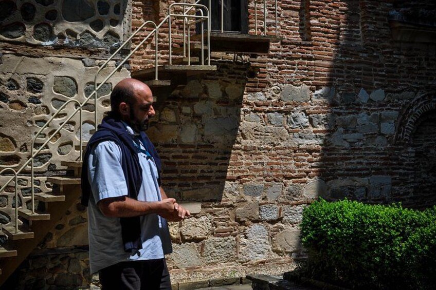 A man standing in front of a stone building with a staircase and a window. 2