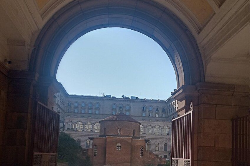 An arched doorway overlooking a historic building with a dome and a smaller structure in front. 4