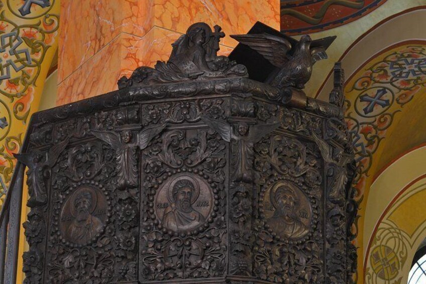 An ornate wooden structure with intricate carvings and religious figures, set against a vibrant mural. 2