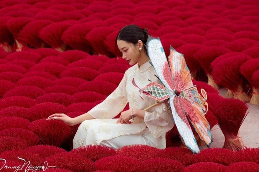 A person sitting amidst red foliage, holding a decorative fan. 4