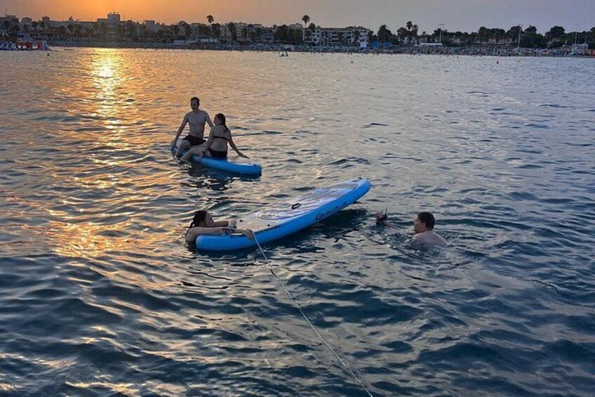 People in the water with blue inflatable boards, a sunset, and a cityscape in the background. 3