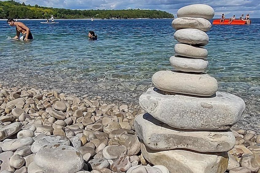 Een stapel stenen op een kiezelstrand, met een meer en boten op de achtergrond. 2