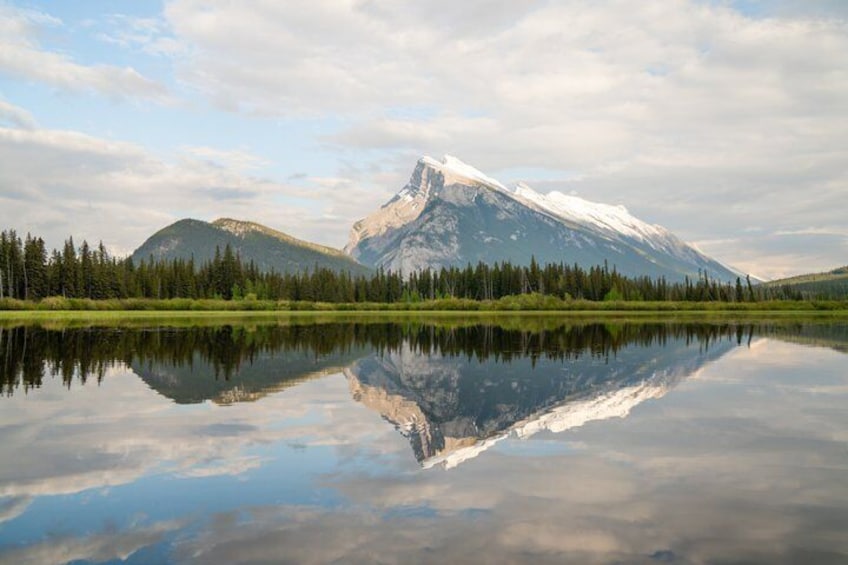 A mountain range with snow-capped peaks, a calm lake reflecting the scenery, and a forested area in the foreground. 4