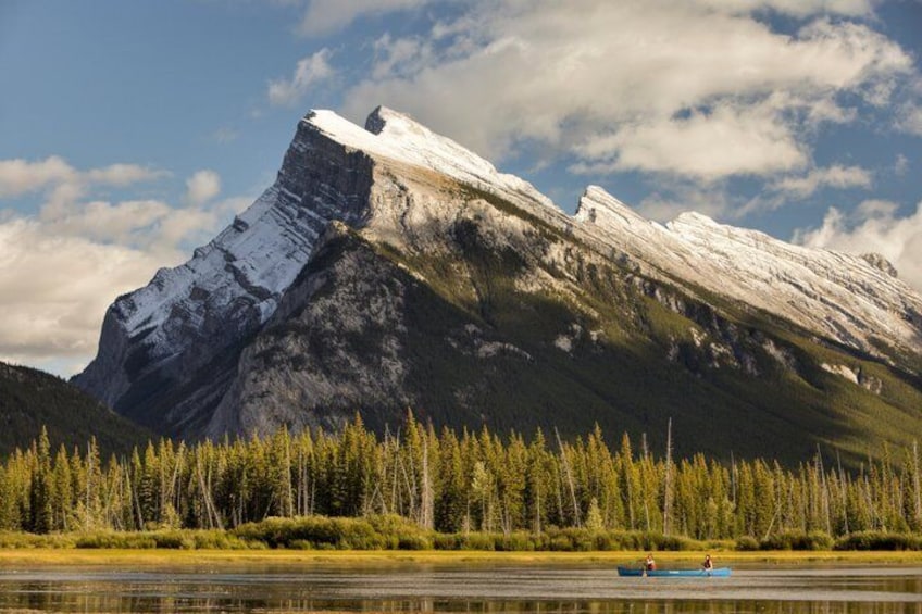 A mountain with a snow-capped peak, a forested area, and a calm river with a canoe. 5