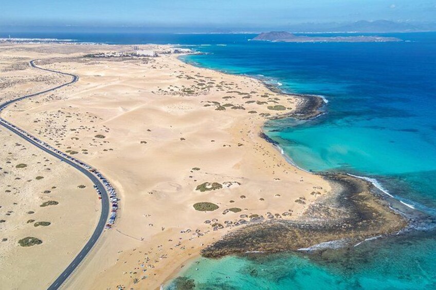 A coastal landscape with a winding road, sandy beach, and clear blue waters. 1