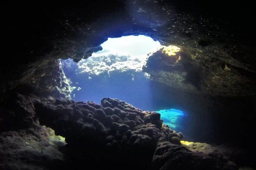 Eine Unterwasserhöhle, durch deren Öffnung Sonnenlicht fällt, umgeben von Felsformationen. 5