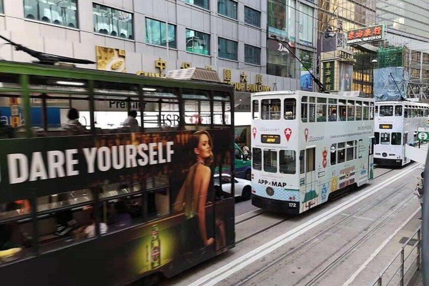 A tram with a large advertisement on the side, a building with a sign in a foreign language, and another tram in the background. 2
