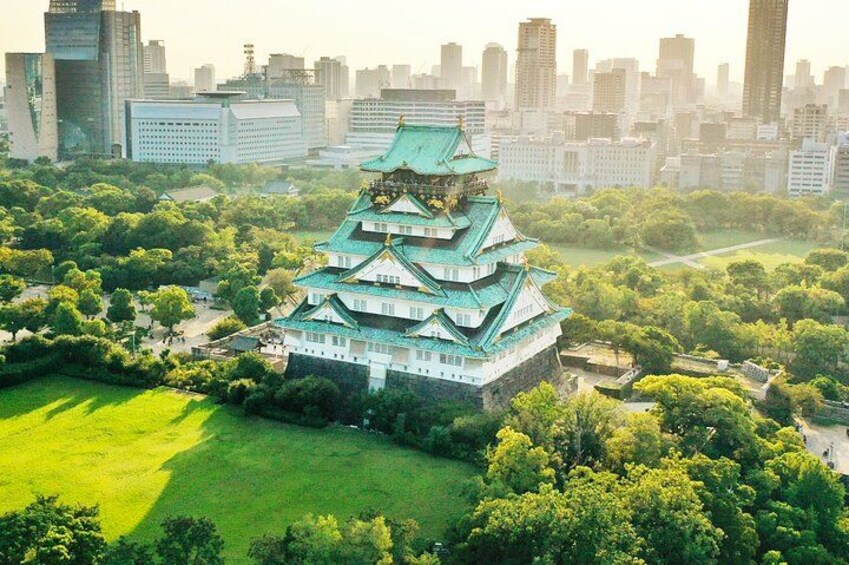 A traditional Japanese castle with multiple tiers, surrounded by lush greenery and a cityscape in the background. 1