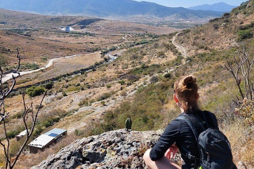 Une personne assise sur un rocher, d’où elle domine une vallée avec un chemin de terre et une végétation clairsemée. 4